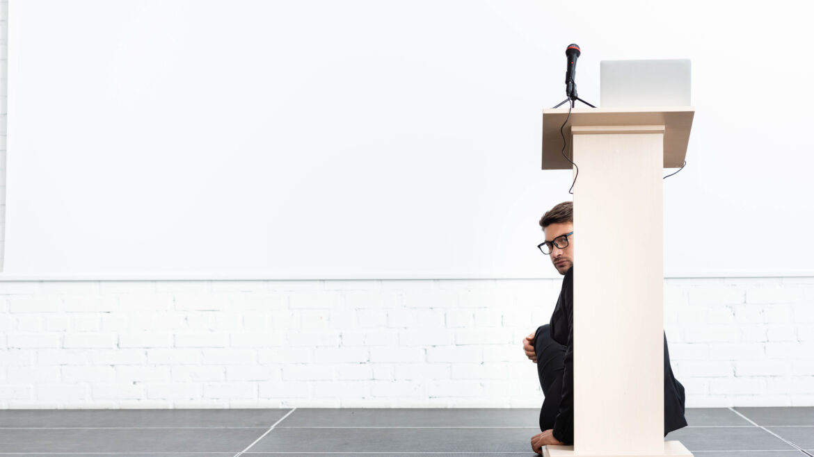 businessman keynote speaker hiding behind podium tribune during conference