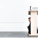businessman keynote speaker hiding behind podium tribune during conference